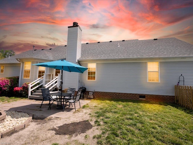 back of property with a chimney, roof with shingles, a yard, and a patio