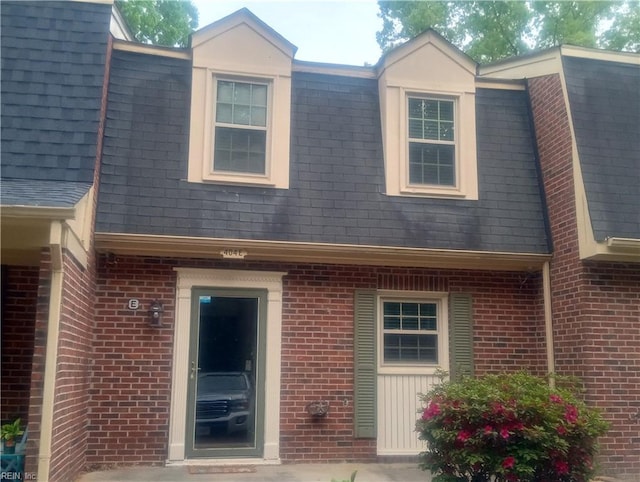 view of front of property with brick siding, a shingled roof, and mansard roof