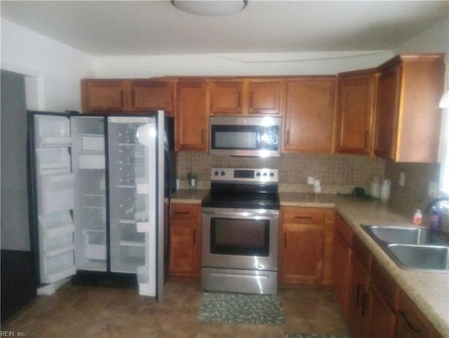 kitchen with tasteful backsplash, brown cabinets, a sink, stainless steel appliances, and light countertops