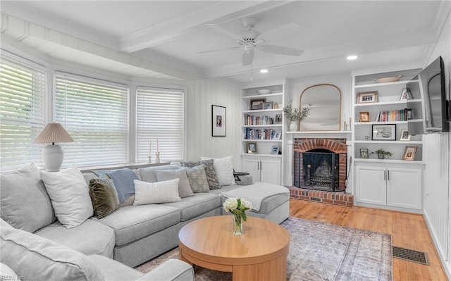 living area featuring a ceiling fan, beamed ceiling, light wood-style flooring, ornamental molding, and visible vents