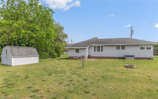 back of property featuring crawl space, a shed, a lawn, an outdoor fire pit, and an outbuilding