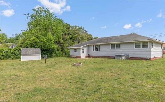 back of property featuring crawl space, a storage shed, a lawn, a fire pit, and an outbuilding