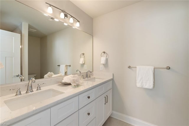 full bath featuring baseboards, a sink, double vanity, and toilet