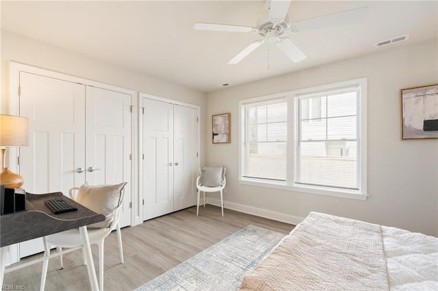 bedroom featuring visible vents, baseboards, wood finished floors, ceiling fan, and multiple closets