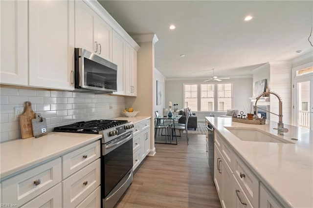 kitchen featuring white cabinets, appliances with stainless steel finishes, ornamental molding, and a sink