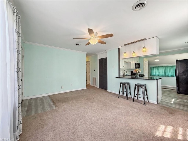 living area featuring carpet, ornamental molding, baseboards, visible vents, and a ceiling fan