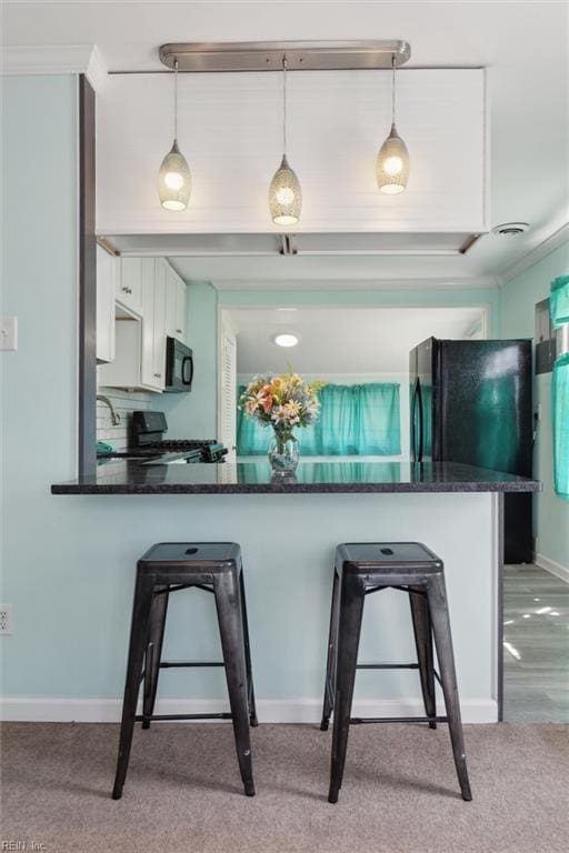 kitchen featuring a breakfast bar area, white cabinetry, black appliances, light carpet, and decorative light fixtures