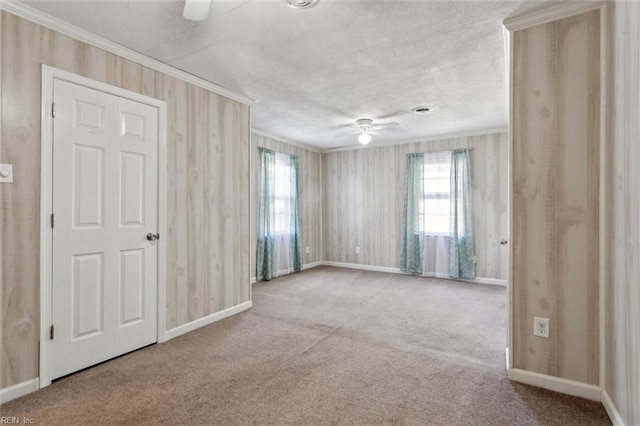 carpeted spare room with a wealth of natural light, baseboards, ornamental molding, and a ceiling fan