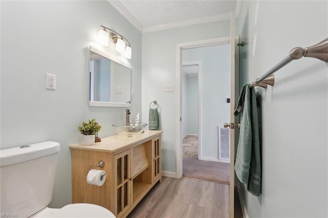 half bath featuring crown molding, baseboards, toilet, wood finished floors, and vanity