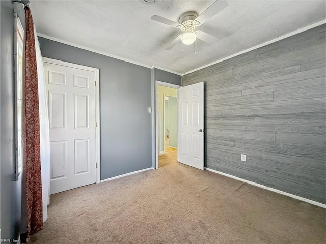 unfurnished bedroom with baseboards, a ceiling fan, wooden walls, and carpet flooring