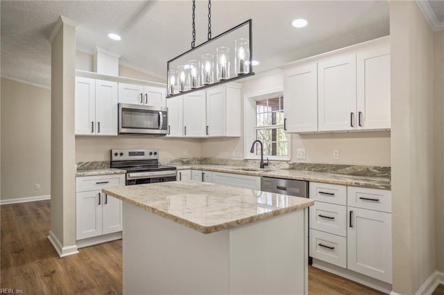 kitchen featuring a center island, a sink, white cabinetry, appliances with stainless steel finishes, and ornamental molding