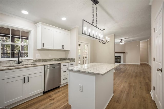 kitchen featuring stainless steel dishwasher, a sink, a kitchen island, white cabinetry, and ceiling fan with notable chandelier