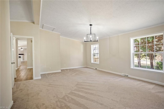 carpeted spare room with a textured ceiling, crown molding, baseboards, and a notable chandelier