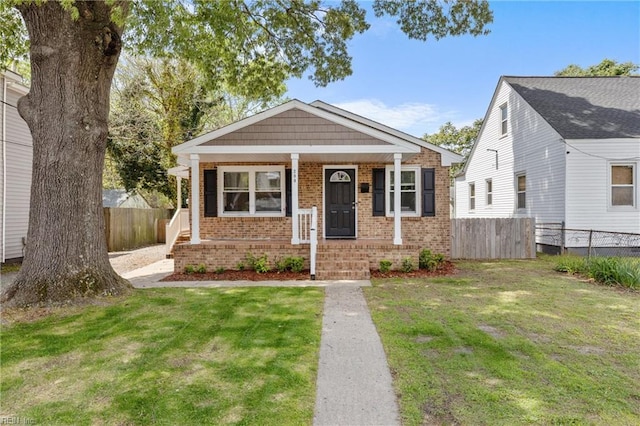 bungalow featuring brick siding, a front yard, and fence