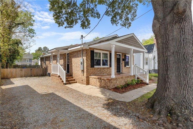 view of front of home with brick siding, fence, and covered porch