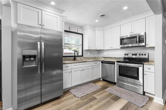 kitchen with light stone counters, a sink, light wood-style floors, stainless steel appliances, and white cabinetry