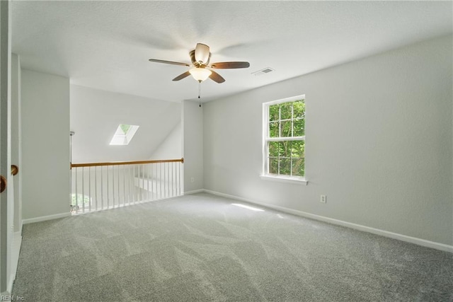carpeted empty room featuring visible vents, a ceiling fan, baseboards, and a skylight