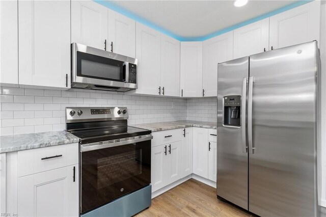 kitchen featuring decorative backsplash, light wood-style floors, white cabinetry, appliances with stainless steel finishes, and light stone countertops