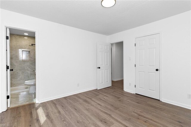 unfurnished bedroom featuring baseboards, ensuite bath, and wood finished floors