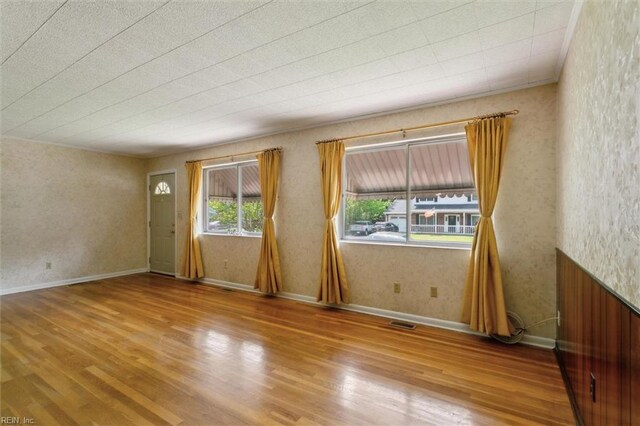 interior space featuring baseboards, wallpapered walls, wood finished floors, and visible vents