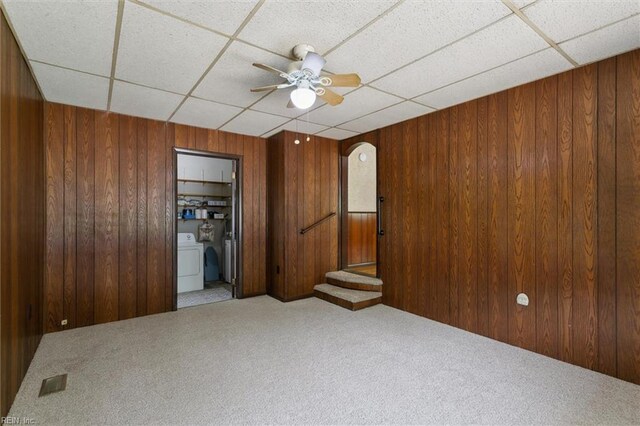 spare room with a paneled ceiling, carpet flooring, wood walls, ceiling fan, and washer / dryer