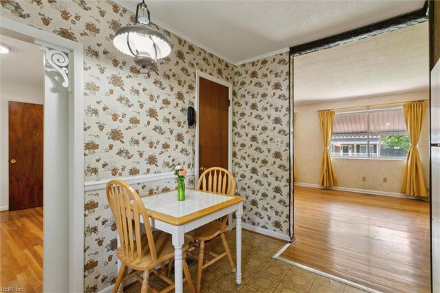 dining room with wallpapered walls, wood finished floors, baseboards, and crown molding