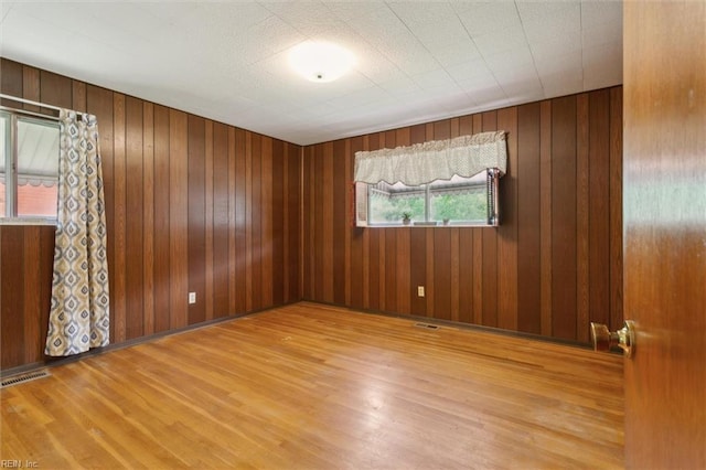 unfurnished room with wood walls, wood finished floors, and visible vents