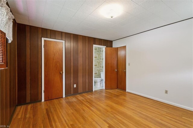 unfurnished bedroom with baseboards, wood finished floors, wooden walls, and ensuite bathroom