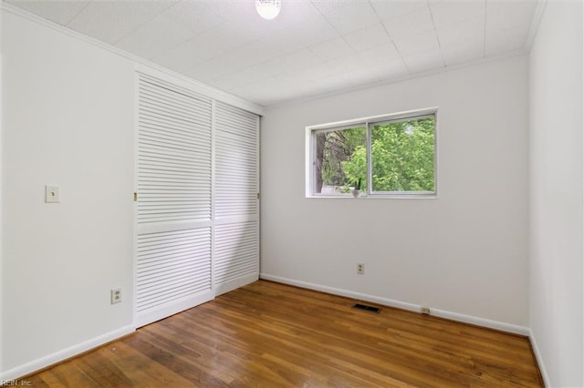 unfurnished bedroom featuring crown molding, wood finished floors, a closet, baseboards, and visible vents