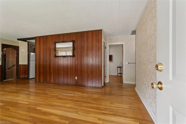 spare room with light wood finished floors, wallpapered walls, and baseboards