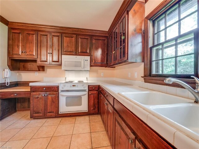kitchen with tile countertops, light tile patterned floors, a sink, white appliances, and glass insert cabinets
