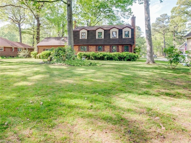 view of front of house with brick siding, a front yard, a gambrel roof, and a chimney