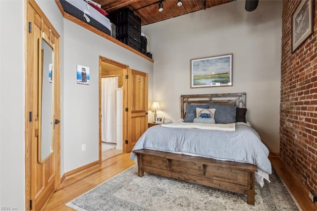 bedroom with wood finished floors, brick wall, wooden ceiling, baseboards, and beam ceiling