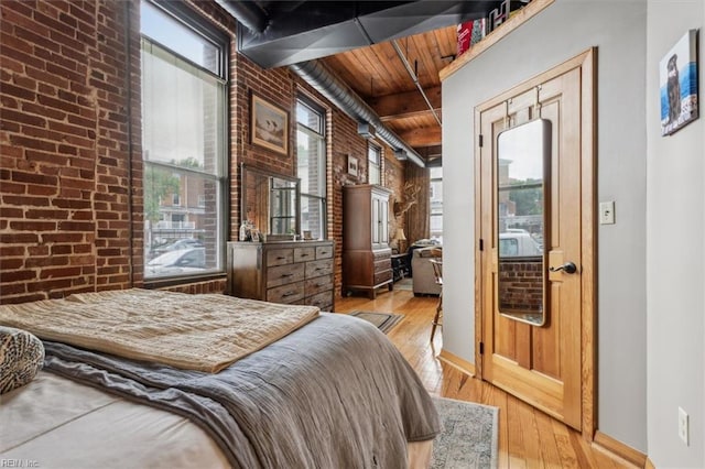 bedroom with brick wall, wooden ceiling, wood finished floors, and baseboards