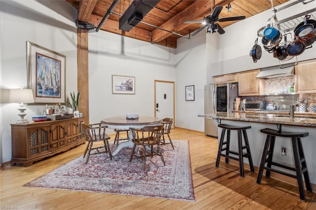 dining space with light wood-style floors, wood ceiling, ceiling fan, beamed ceiling, and a high ceiling