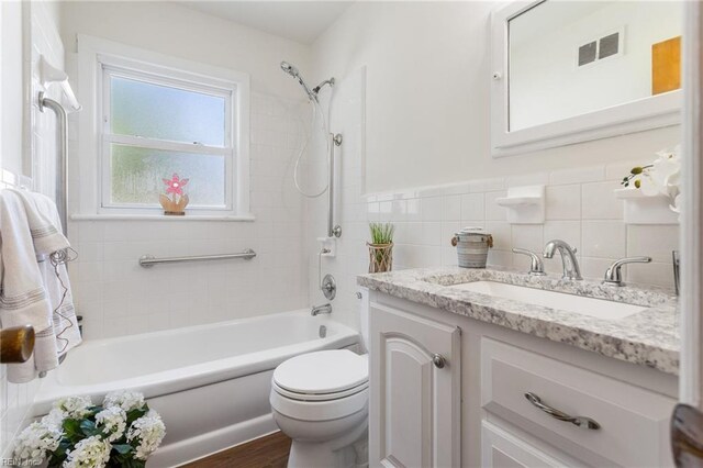 bathroom featuring tile walls, vanity, toilet, visible vents, and tub / shower combination
