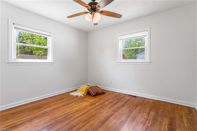 empty room featuring a ceiling fan, visible vents, wood finished floors, and baseboards