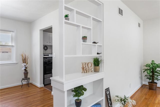 hallway with light wood-style floors, visible vents, and baseboards