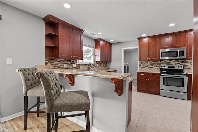 kitchen featuring light stone countertops, appliances with stainless steel finishes, a peninsula, recessed lighting, and tasteful backsplash