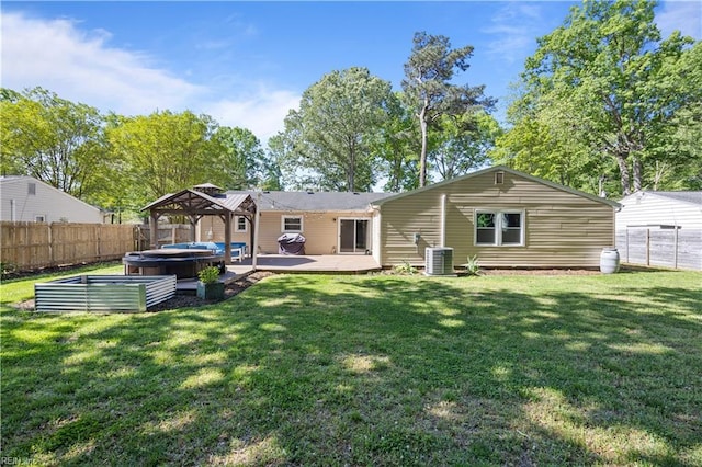rear view of house featuring a fenced backyard, a lawn, a gazebo, and a hot tub