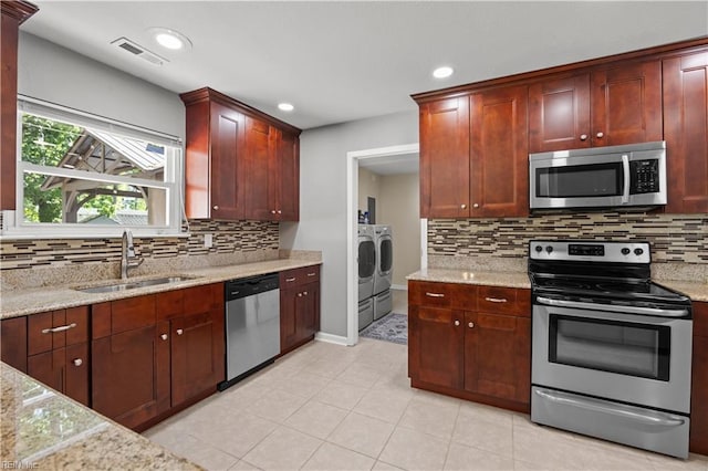 kitchen featuring backsplash, visible vents, a sink, stainless steel appliances, and washer and dryer