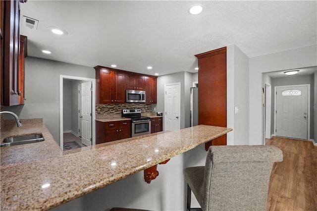 kitchen with a sink, light stone counters, light wood finished floors, a peninsula, and stainless steel appliances