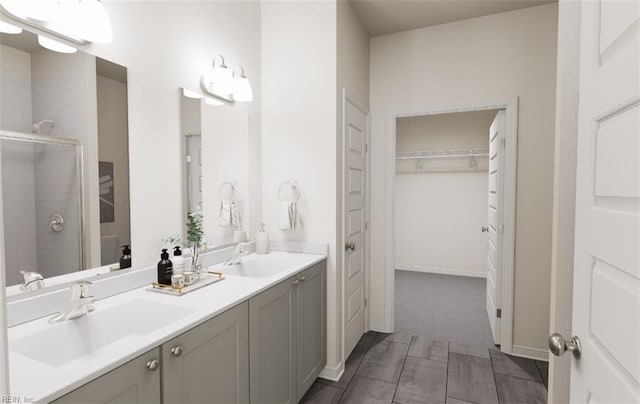 bathroom with double vanity, a walk in closet, a sink, and a stall shower