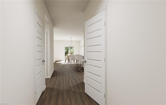 hall featuring dark wood-style flooring, baseboards, and a chandelier