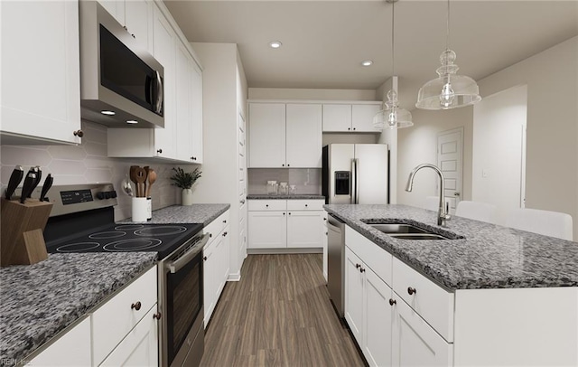 kitchen featuring white cabinets, a sink, dark stone counters, stainless steel appliances, and a center island with sink