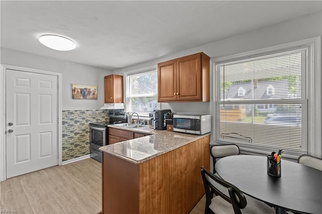 kitchen with a sink, appliances with stainless steel finishes, exhaust hood, a peninsula, and brown cabinetry