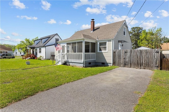 bungalow-style house featuring a sunroom, a front yard, a chimney, roof with shingles, and fence