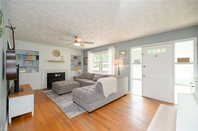 living area with light wood finished floors, a textured ceiling, built in shelves, ceiling fan, and a fireplace