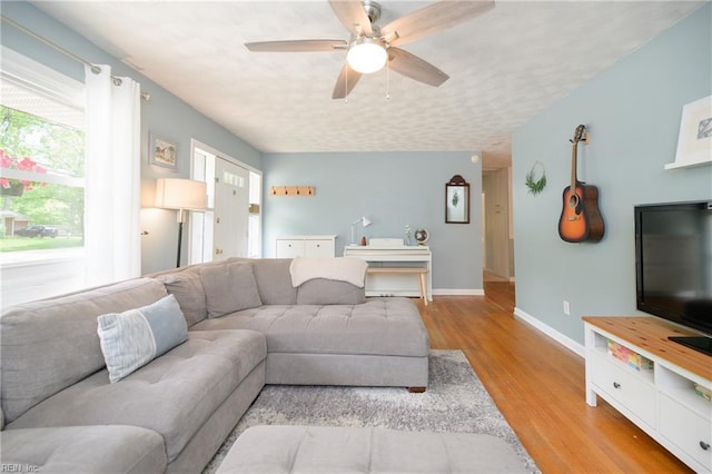 living area with baseboards, a ceiling fan, and light wood-type flooring