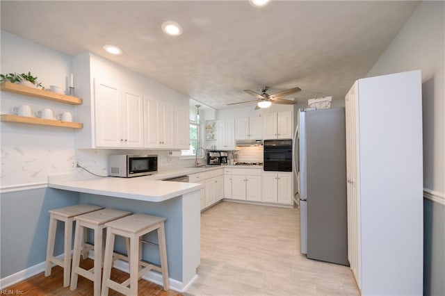 kitchen featuring stainless steel appliances, a peninsula, a sink, decorative backsplash, and under cabinet range hood